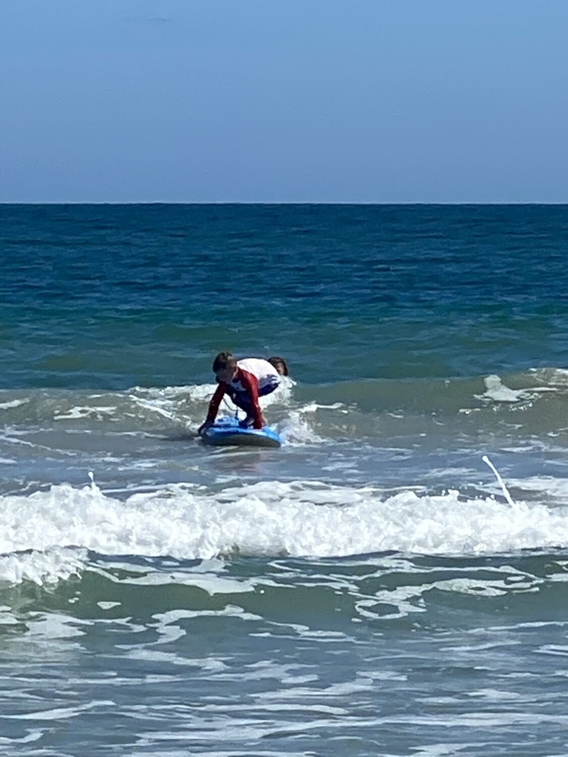 A child rides a wave on his surf board in the ocean.