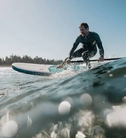 A person surfs energetically on a wave under a clear blue sky. The scene is dynamic, conveying excitement and the beauty of a sunny day at the ocean.