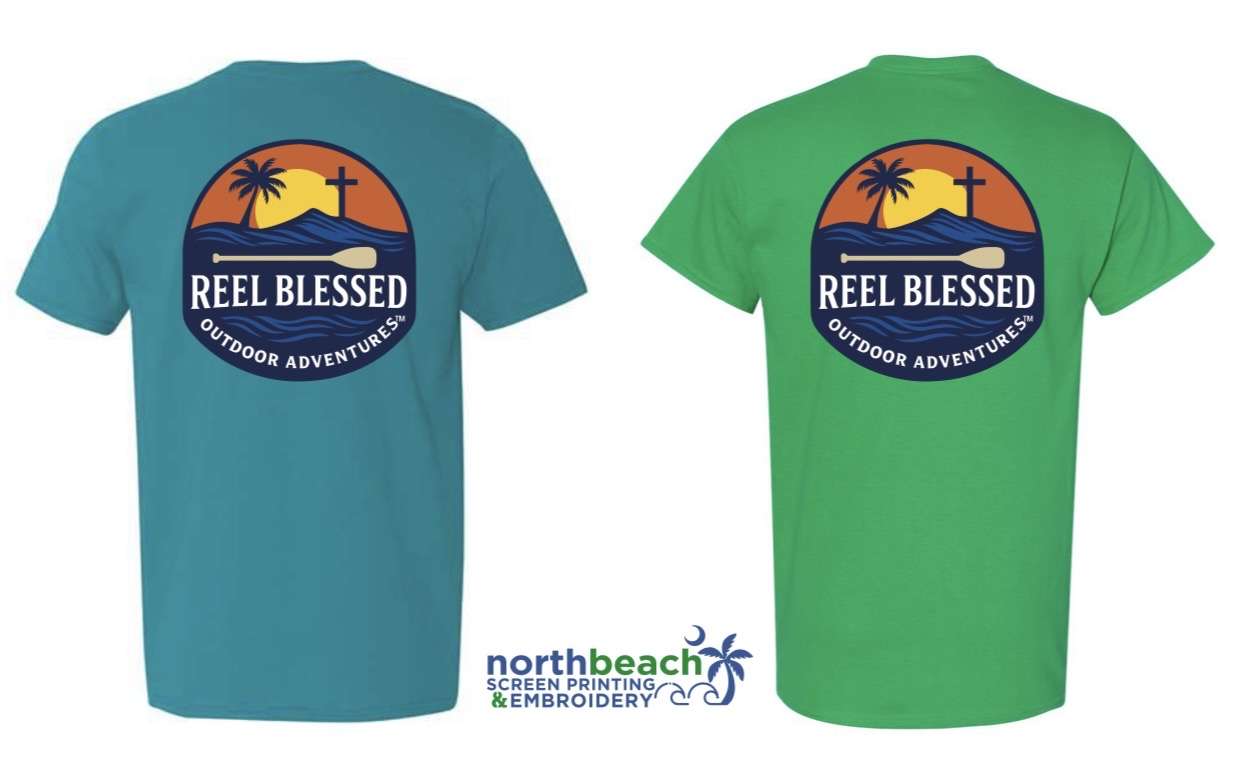 The Reel Blessed Adventures logo on the back of a shirt. It has a sunset framed with a palm tree and a cross. There’s a paddle on top of reel blessed with a dark blue bottom to the logo